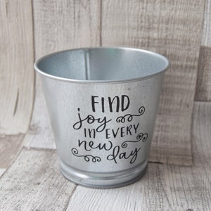 May include: A silver metal planter with the text "FIND joy in EVERY new day" printed on the side.
