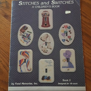 May include: A book titled "Stitches and Switches: A Children's Book" by Fond Memories, Inc. The book features illustrations of light switch covers with various designs, including a gumball machine, a cat, a kite, and a girl in a dress. The book is designed for 18 count fabric.