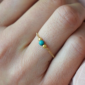 Puede incluir: Un delicado anillo de cadena de oro con una sola piedra turquesa. El anillo se lleva en un dedo.
