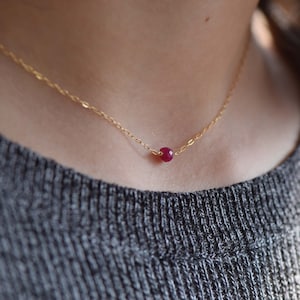 Op de afbeelding: Een delicate gouden ketting met een enkele, kleine, ronde, rode edelsteen hanger.