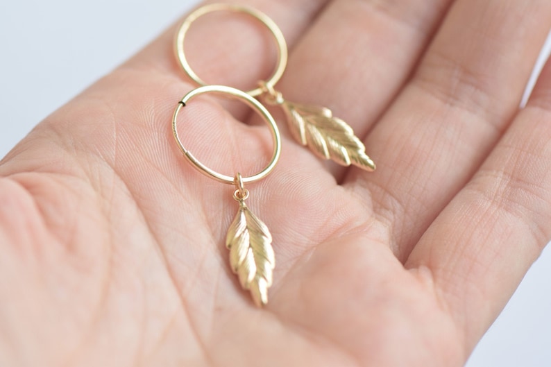 May include: Gold hoop earrings with a delicate leaf charm dangling from each hoop.