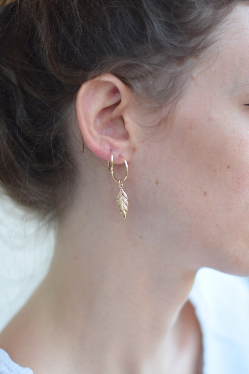 May include: Gold hoop earrings with a small gold leaf charm dangling from one earring.