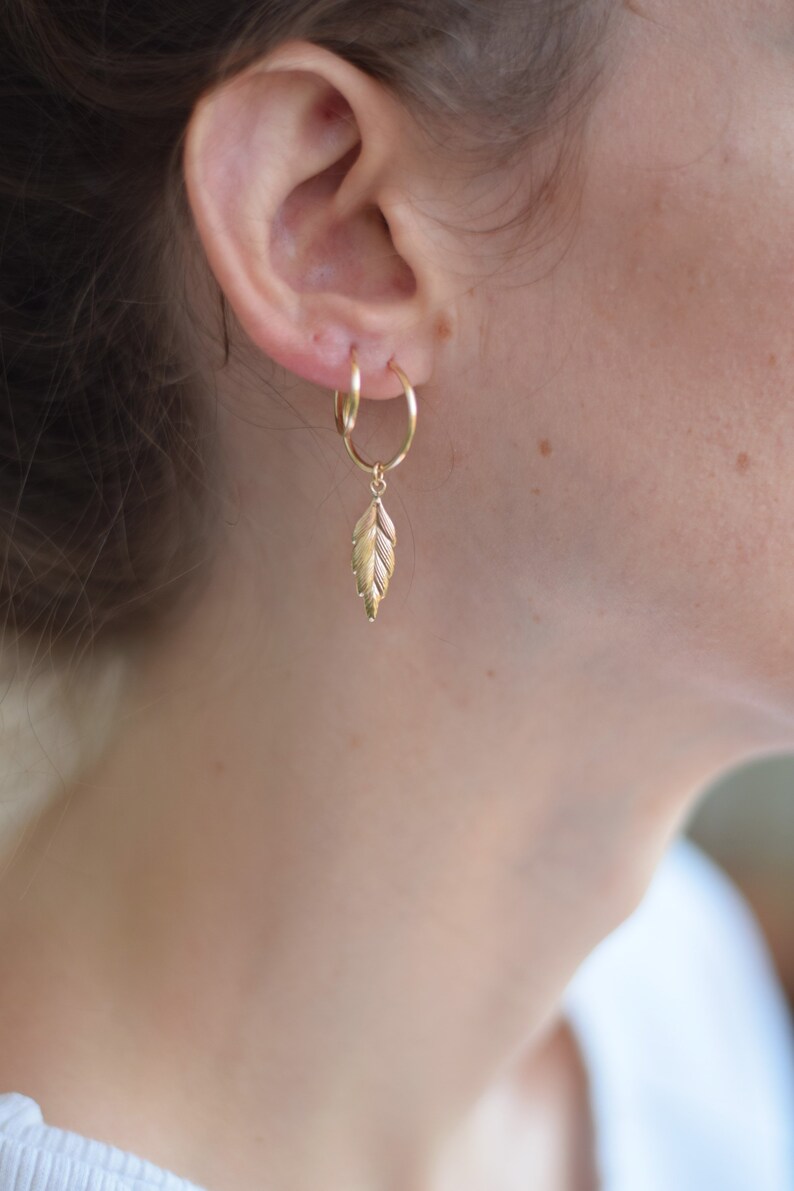 May include: Gold hoop earrings with a small gold leaf charm dangling from one earring.
