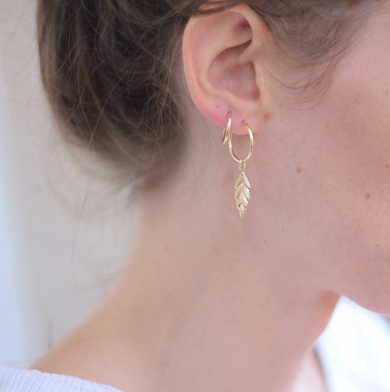 May include: Gold hoop earrings with a small gold leaf charm dangling from one earring.