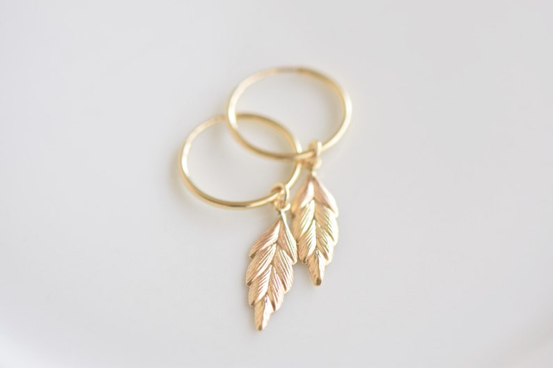 May include: A pair of gold hoop earrings with small leaf charms dangling from each hoop.