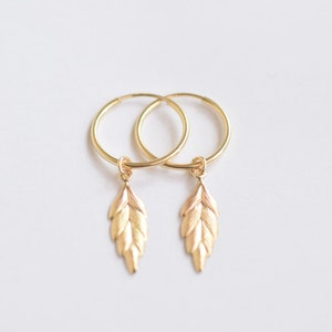 May include: Gold hoop earrings with a small leaf charm dangling from each hoop.