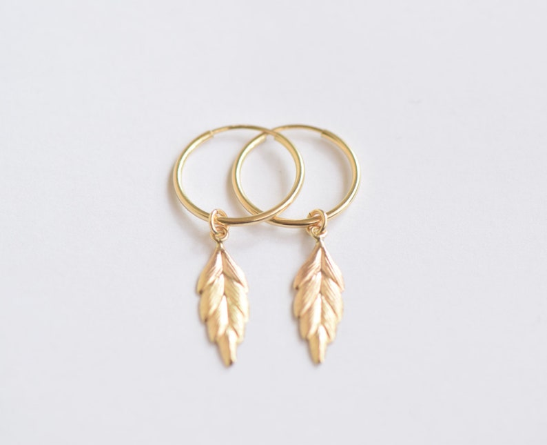 May include: Gold hoop earrings with a small leaf charm dangling from each hoop.