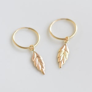 May include: A pair of gold hoop earrings with a small gold leaf charm dangling from each hoop.