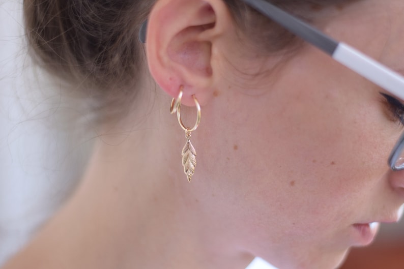 May include: Gold hoop earrings with a small gold leaf charm dangling from one earring.