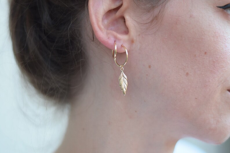 May include: Gold hoop earrings with a gold leaf charm dangling from the bottom.