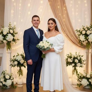Könnte beinhalten: Ein Hochzeitsfoto eines Paares. Die Frau trägt ein weißes schulterfreies Kleid und einen Schleier und hält einen Blumenstrauß. Der Mann trägt einen marineblauen Anzug mit hellblauer Krawatte. Weiße Blumengestecke und ein dekorativer Hintergrund.