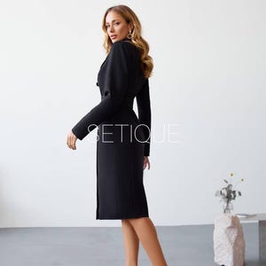 Peut inclure: Une robe noire avec un haut de style blazer et une jupe mi-longue. La robe a une taille ceintur&eacute;e et des boutons. L'image comprend le texte "SETIQUE". Le mod&egrave;le porte des talons hauts noirs.
