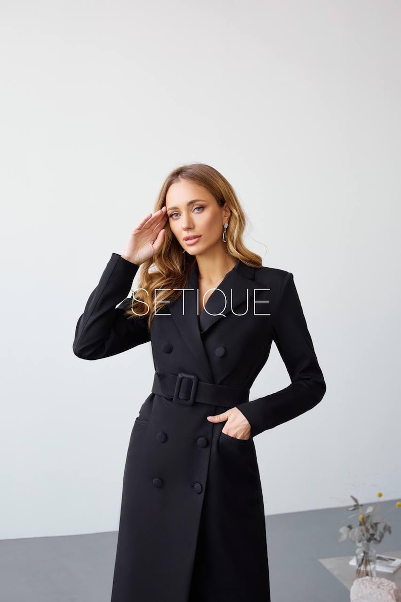 Peut inclure: Robe blazer noire &agrave; double boutonnage, ceinture et poches. La robe a des manches longues et un col crant&eacute;. Le mot "SETIQUE" est imprim&eacute; sur la robe.