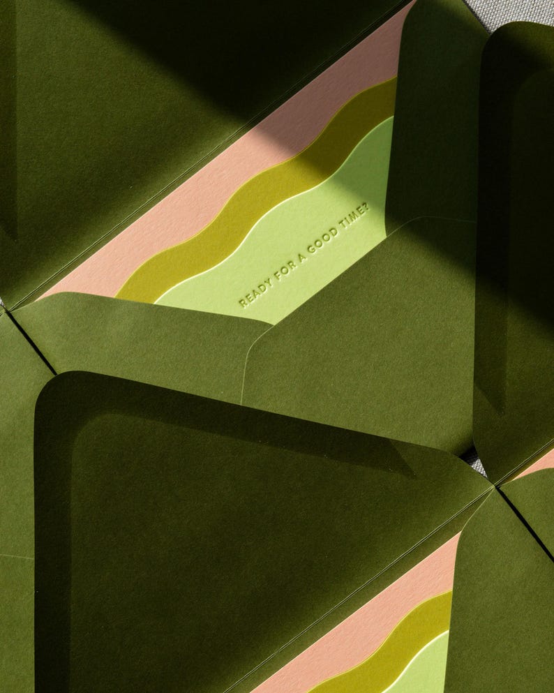 May include: A set of dark olive green envelopes with open flaps revealing a light green interior liner. The liner features wavy bands of pink and lime green, with the text READY FOR A GOOD TIME? embossed in a clean, sans-serif font.