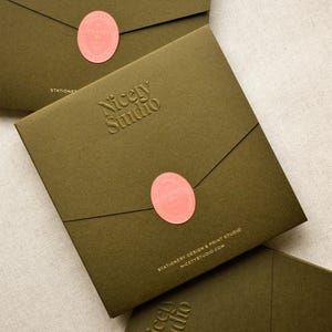 May include: Three square olive green envelopes featuring a debossed Nicety Studio logo. Each envelope is sealed with a coral oval sticker printed with the text Printed by Hand. The bottom envelope displays the text Stationery Design & Print Studio.