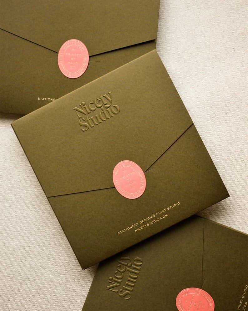 May include: Three square olive green envelopes featuring a debossed Nicety Studio logo. Each envelope is sealed with a coral oval sticker printed with the text Printed by Hand. The bottom envelope displays the text Stationery Design & Print Studio.