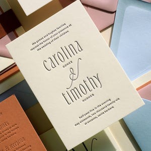 May include: An off-white wedding invitation card with dark embossed text reading Carolina Gomez and Timothy Hughes, surrounded by various colored envelopes in shades of pink, blue, and terracotta, featuring a formal event announcement.
