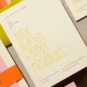 May include: A cream-colored wedding invitation card featuring embossed yellow lettering that reads THE WEDDING OF KATIE KLASSEN & BERRY MASHBURN, with pink text indicating the date February 28, 2026, at 4:30 PM and the location El Mangroove Hotel, Guanacaste, Costa Rica.