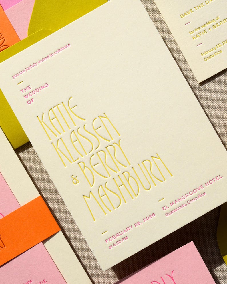 May include: A cream-colored wedding invitation card featuring embossed yellow lettering that reads THE WEDDING OF KATIE KLASSEN & BERRY MASHBURN, with pink text indicating the date February 28, 2026, at 4:30 PM and the location El Mangroove Hotel, Guanacaste, Costa Rica.