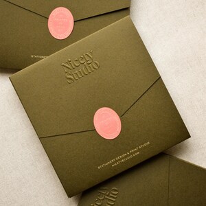 May include: Three square olive green envelopes featuring a debossed Nicety Studio logo. Each envelope is sealed with a coral oval sticker printed with the text Printed by Hand. The bottom envelope displays the text Stationery Design & Print Studio.