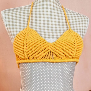 Può includere: Un top halter in crochet giallo con un design triangolare. Il top è realizzato con un filato spesso e testurizzato e presenta un delicato dettaglio a frangia.