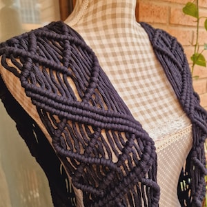 以下が含まれることがあります： 幾何学模様の黒いクロシェベスト。厚手の糸で作られており、ゆったりとした流れるようなフィット感です。