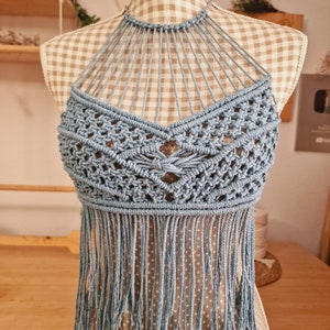 Puede incluir: Un top halter de crochet azul claro con detalles de flecos. El top está hecho con un delicado patrón de punto abierto.