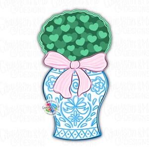 May include: A blue and white ceramic vase with a green plant with heart-shaped leaves. The vase has a pink bow around the neck.