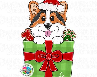 May include: A digital illustration of a Corgi dog wearing a Santa hat, peeking out of a green gift box tied with a red bow. The box contains a bone-shaped cookie and a paw print cookie. The image includes the text "Grayson & Me Designs".
