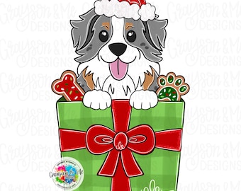 May include: A digital illustration of a dog wearing a Santa hat, peeking out of a green gift box tied with a red bow. The dog has gray, white, and brown fur. The gift box contains a bone-shaped cookie and a paw print cookie. The text "Grayson & Me Designs" is visible.