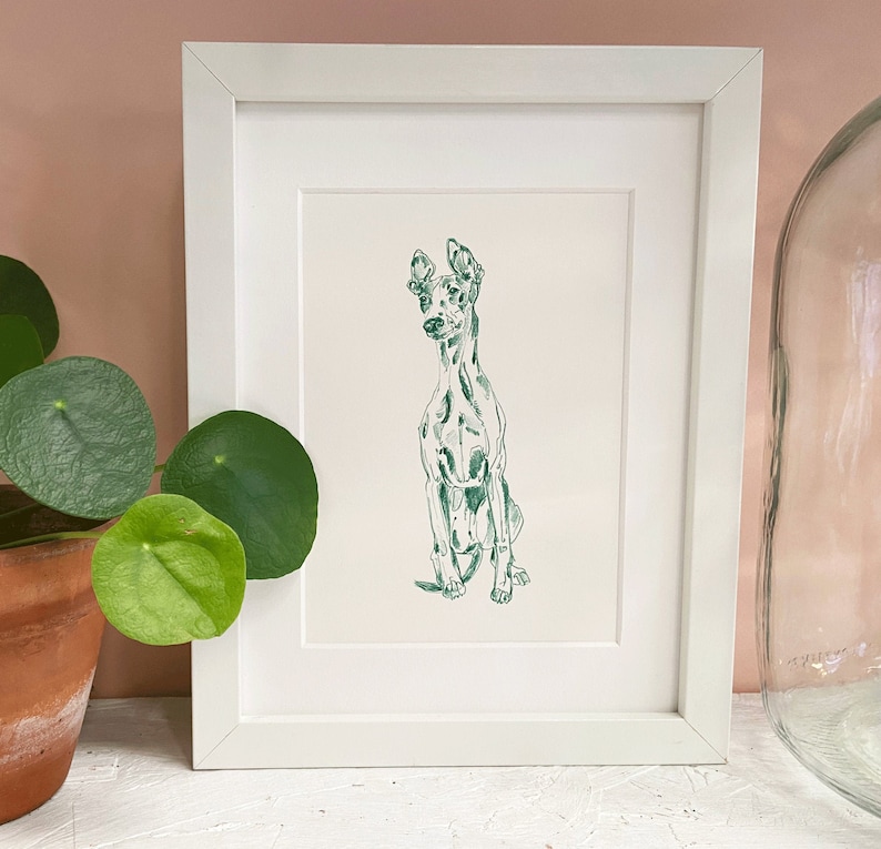May include: A framed illustration of a green and white dog sitting in a white frame. The dog is drawn in a simple, stylized manner.