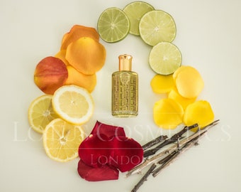 May include: A perfume bottle with a gold cap and a patterned design, surrounded by colorful elements. Slices of lemon and lime, rose petals, and small twigs create a vibrant, circular arrangement. The overall aesthetic is fresh and natural.