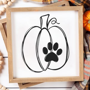 May include: A black and white illustration of a pumpkin with a paw print in the center. The pumpkin is on a white background and is framed in a wooden frame.