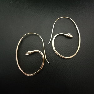 Op de afbeelding: Een paar gouden slang creolen. De oorbellen zijn gemaakt van dun, gehamerd metaal en hebben een slangkop ontwerp.