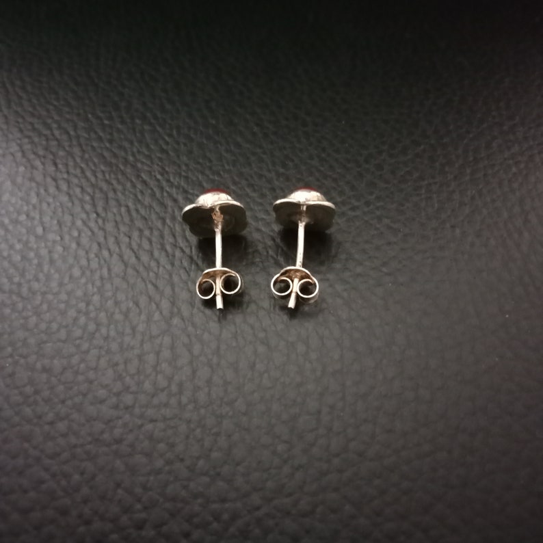 K&ouml;nnte beinhalten: Ein Paar silberne Ohrstecker mit roten Edelsteinen. Die Ohrringe haben ein schlichtes Design und sind perfekt f&uuml;r den Alltag.