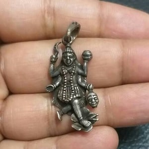 Può includere: Un ciondolo d'argento raffigurante una divinità con molte braccia, probabilmente una dea indù. Il ciondolo presenta dettagli intricati, tra cui una base floreale e una piccola testa mozzata. È sospeso da un piccolo anello.