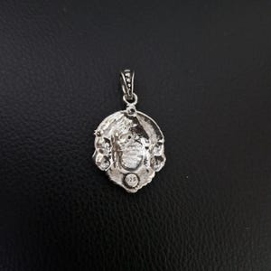 May include: Silver pendant featuring an intricate design of a face surrounded by floral motifs. The reverse of the pendant is stamped with the number "925".