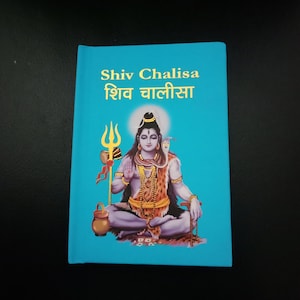 Könnte beinhalten: Ein türkisfarbenes Buch mit dem Titel "Shiv Chalisa" in Englisch und Hindi. Das Cover zeigt eine sitzende Illustration einer Gottheit mit einer Schlange, die einen Dreizack und einen Topf hält. Die Gottheit ist mit Goldschmuck und einem Leopardenmuster-Kleidungsstück geschmückt.