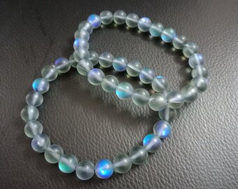 Op de afbeelding: Twee regenboogkleurige blauwe en witte kralen armbanden. De kralen zijn rond en hebben een gladde, gepolijste afwerking.