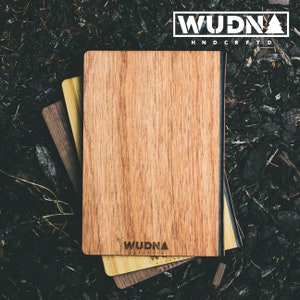 May include: A stack of three wooden notebooks with a black leather-like binding. The top notebook has the word "WUDNA" printed on the front in a white sans-serif font. The text "HANDCRAFTED" is printed below the word "WUDNA" in a smaller white sans-serif font.