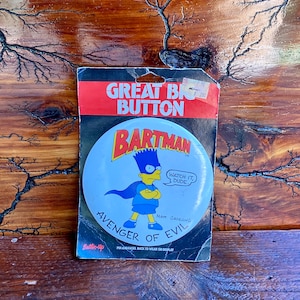 May include: A blue and yellow Bartman button with the text "Watch it, dude" and "Avenger of Evil". The button is on a white background with a red border.