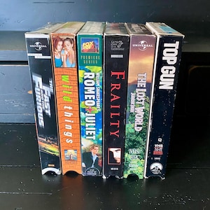 May include: A collection of VHS tapes, including "The Fast and the Furious", "Wild Things", "Romeo + Juliet", "Frailty", "The Lost World: Jurassic Park", and "Top Gun".