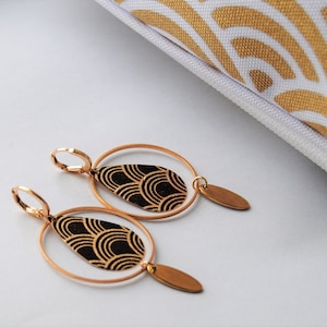 May include: A pair of gold hoop earrings with a black and gold teardrop pendant. The pendant has a geometric pattern.