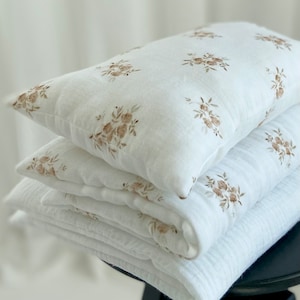 Puede incluir: Una pila de tela de muselina blanca con un estampado floral marrón. La tela está doblada y superpuesta sobre un taburete negro.