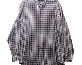 Puede incluir: Una camisa abotonada de manga larga con un estampado de cuadros rojos, blancos y azul marino. La camisa tiene cuello abotonado y un pequeño logo rojo en el pecho. La camisa está colgada de una percha negra.
