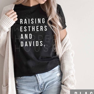 May include: Black t-shirt with white text that reads "Raising Esthers and Davids".