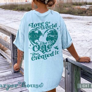 May include: Light blue t-shirt with a distressed green graphic that says "Love the World like the One who Created it". The graphic features a heart-shaped outline of the Earth with a dove.