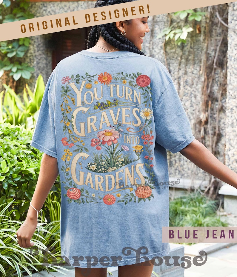 May include: A light blue t-shirt with the text "You Turn Graves Into Gardens" in a floral design. The shirt has short sleeves and a relaxed fit. The words "Original Designer" are printed at the top.