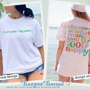 May include: White t-shirt with a green design on the front that says "God's plan > my plan". The back of the shirt has a colorful design with the text "Do more of what makes you God happy".