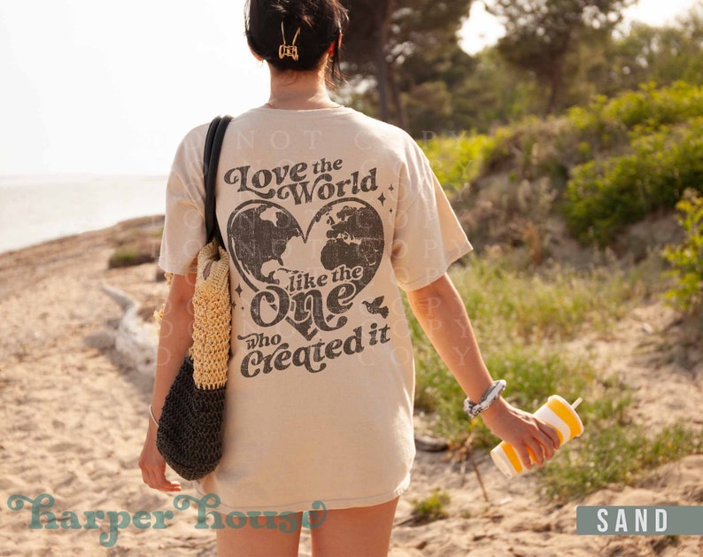 May include: A beige t-shirt with a graphic print of a heart-shaped world with the text "Love the World like the One who Created it".